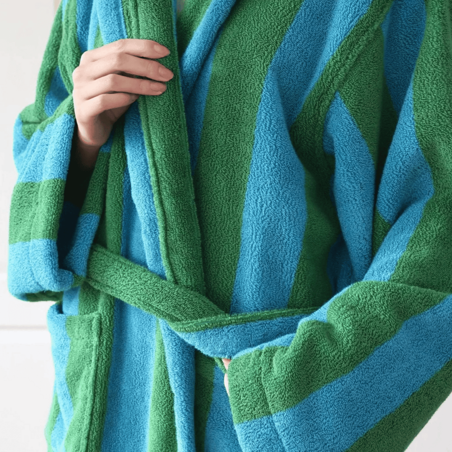 Green and blue striped robe held by a hand against a white background