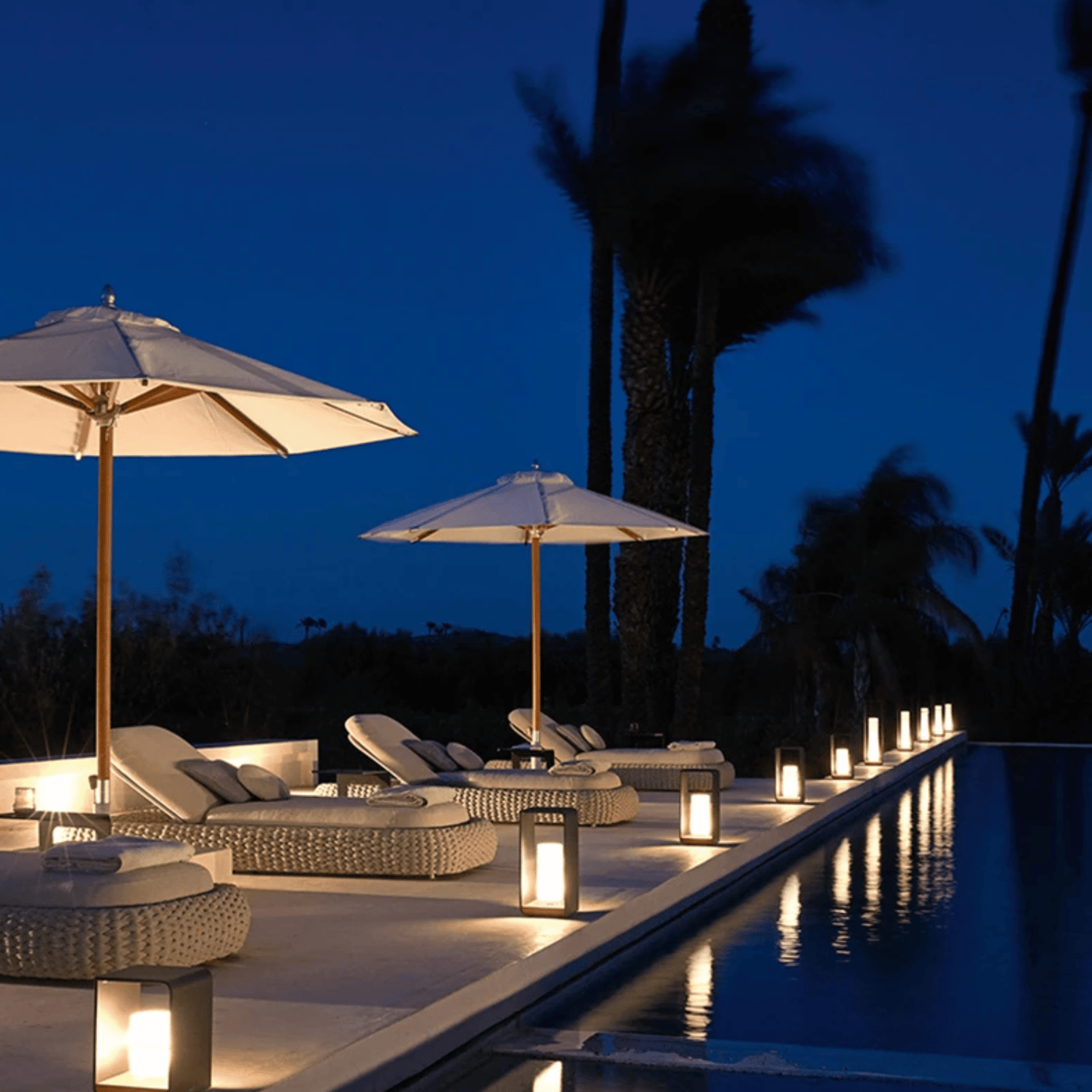 Poolside area with lounge chairs, umbrellas, and candles at night.