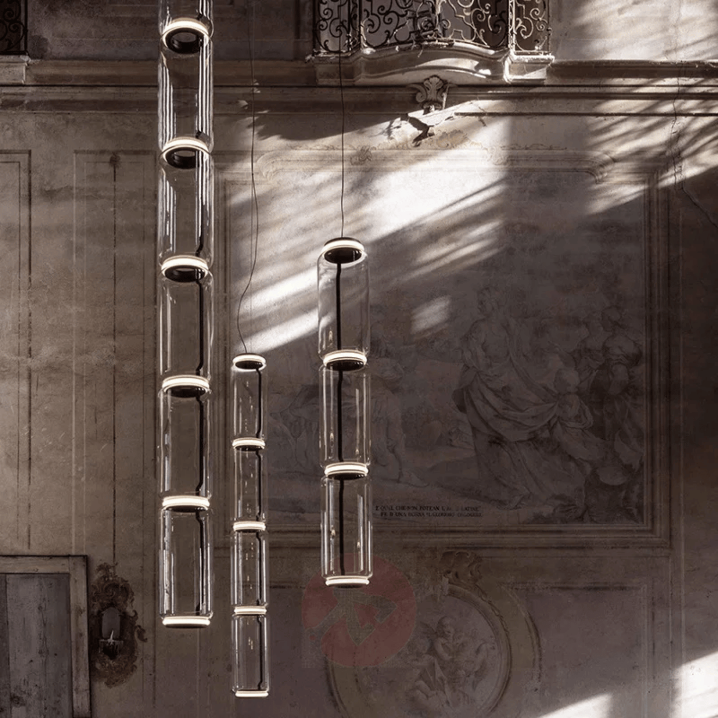 Decorative metal wall art with cylindrical elements against a textured wall.