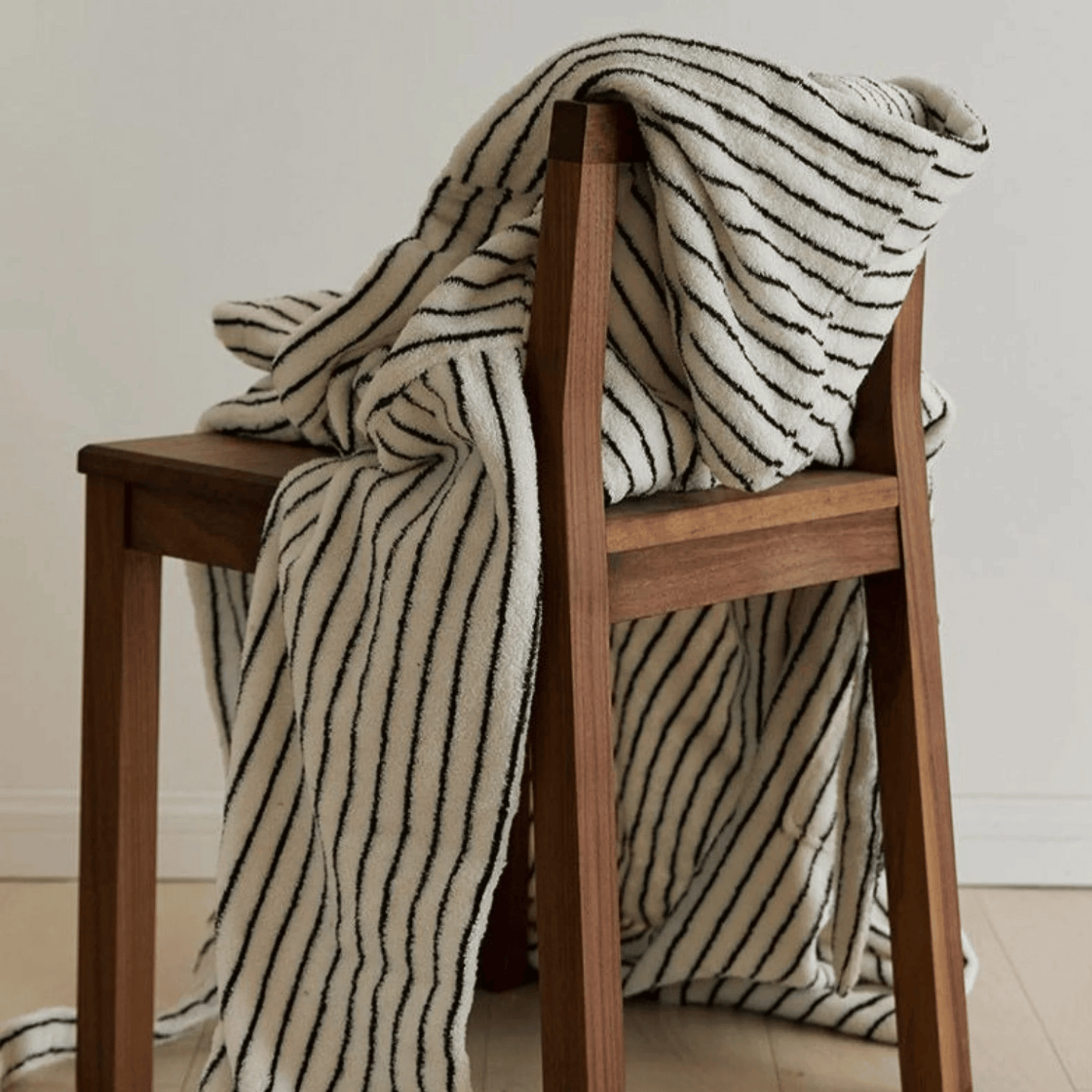 Striped blanket draped over a wooden chair against a neutral background