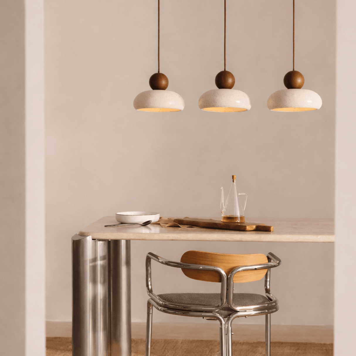 Modern dining area with a table, chair, and pendant lights in a neutral setting.