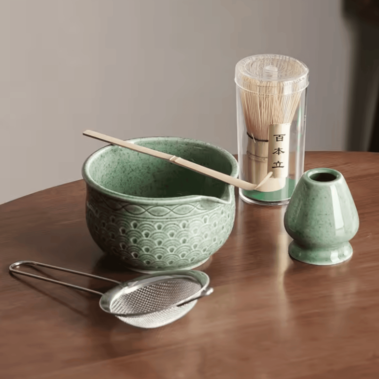 Green ceramic tea set with a bowl, whisk, scoop, and container on a wooden surface.