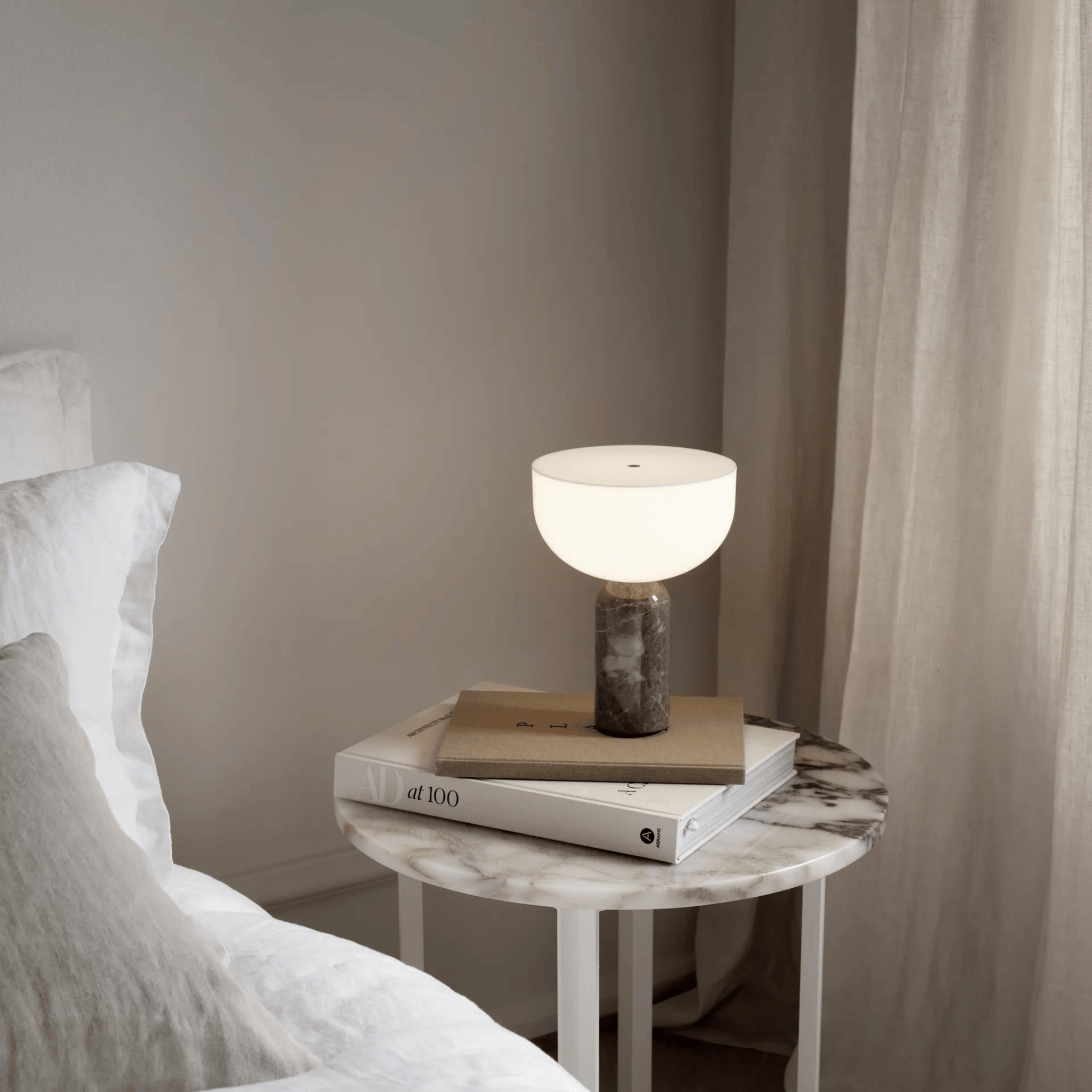 Modern table lamp on a marble side table next to a bed with neutral tones.