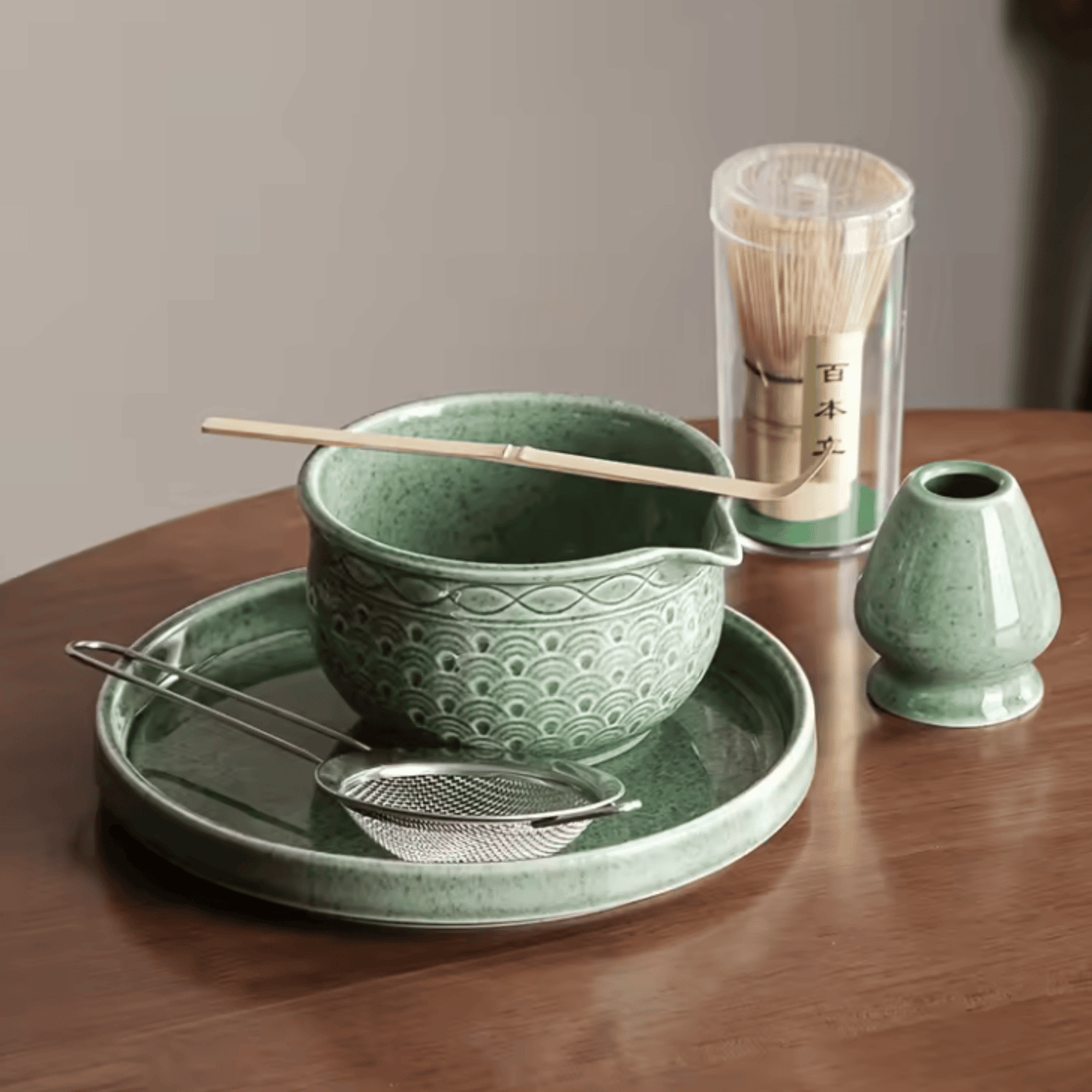 Green ceramic tea set with bowl, tray, whisk, and holder on a wooden table.