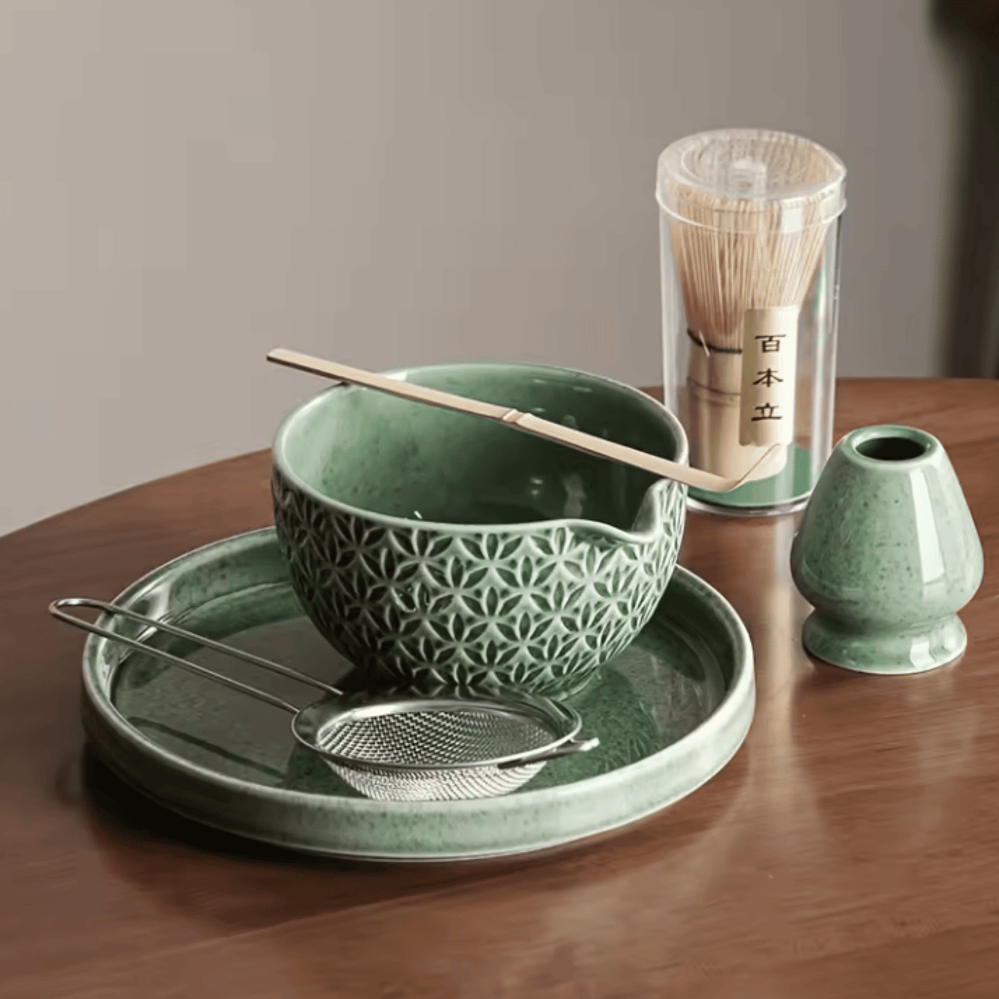 Green ceramic tea set with bowl, spoon, and container on a wooden table.