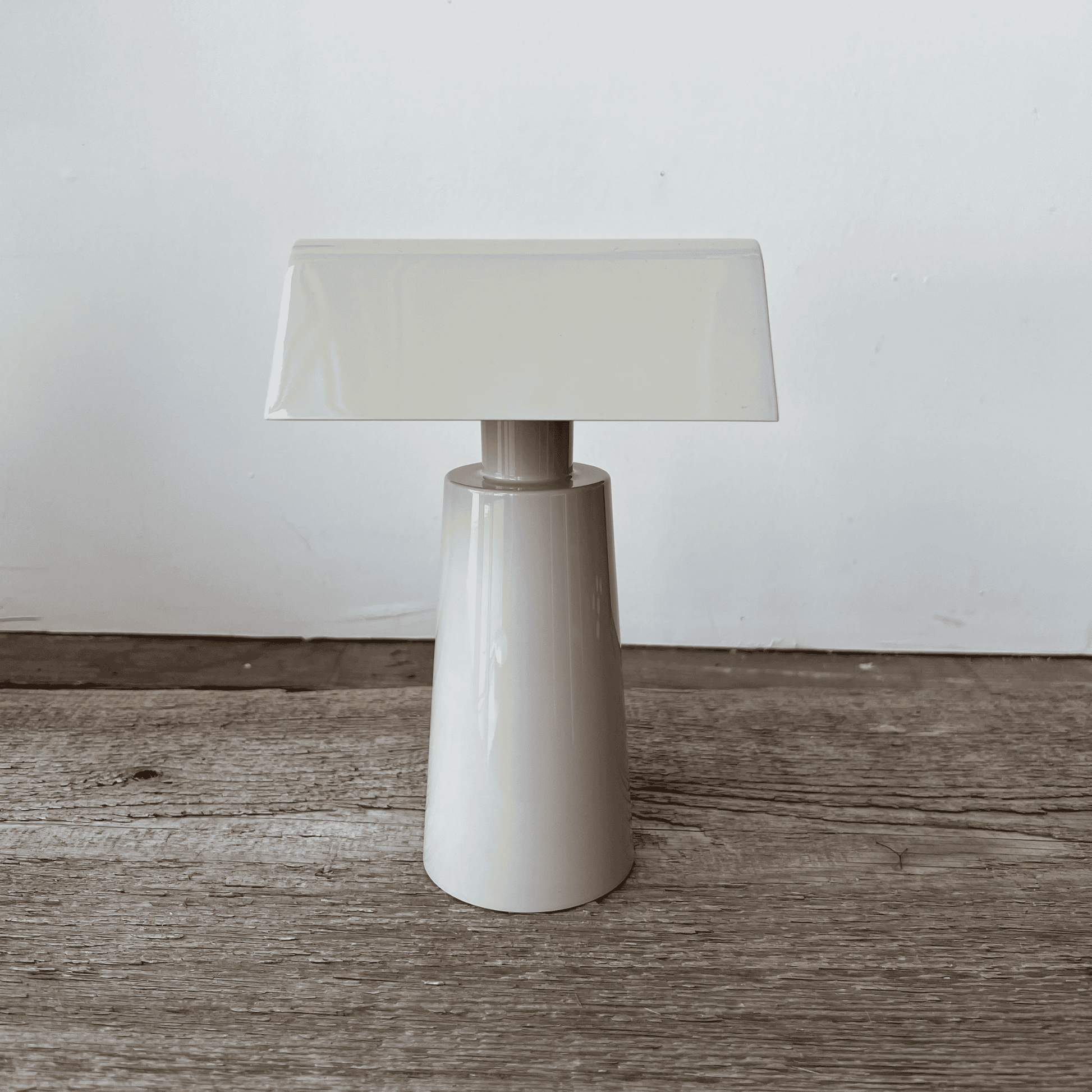 White table lamp with a beige shade on a wooden surface against a white wall