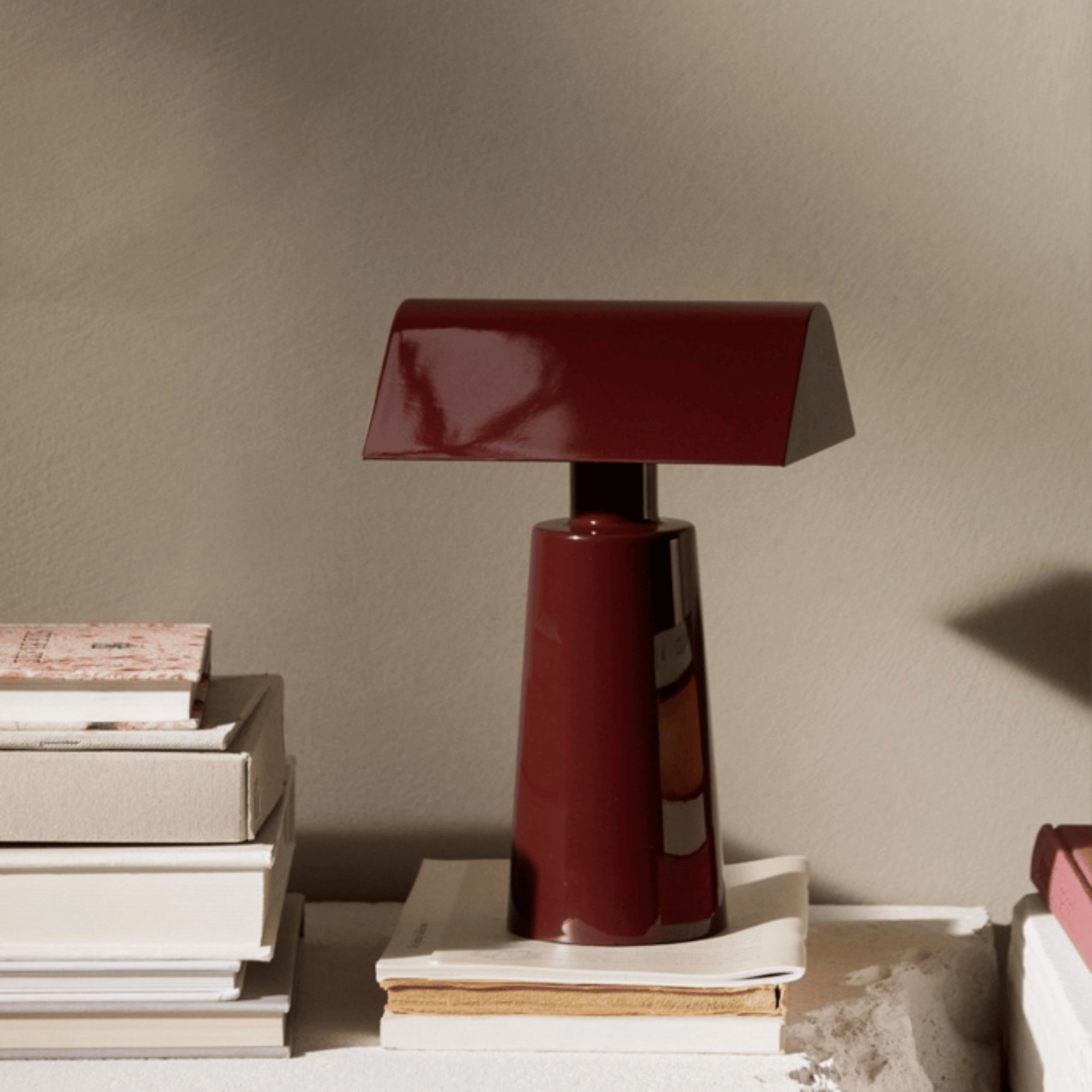 Red table lamp on a stack of books against a beige wall