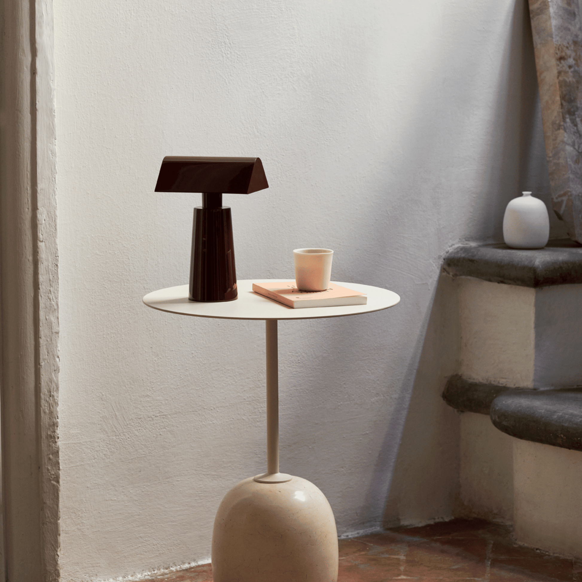 Small round table with a lamp and cup against a textured wall.