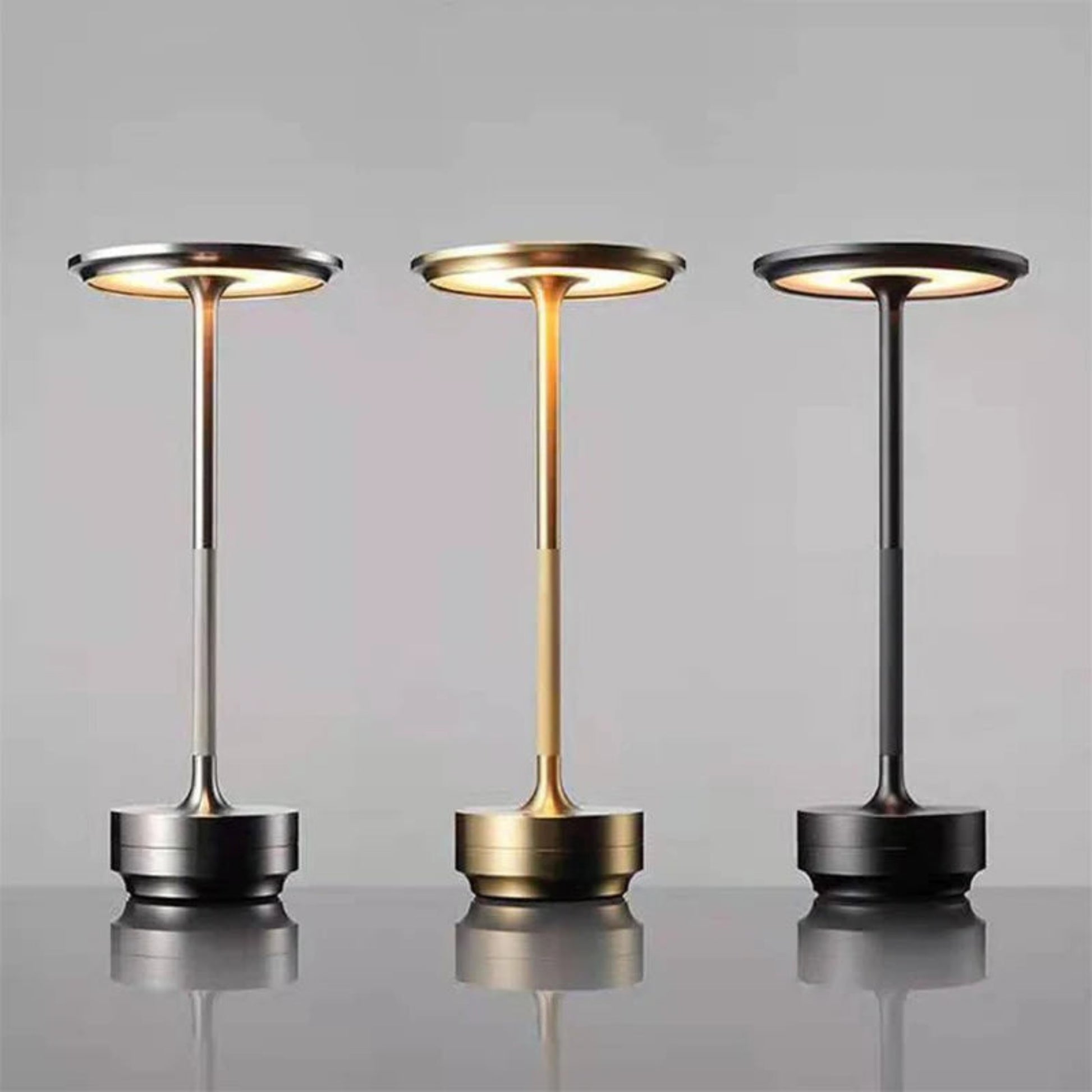 Three modern table lamps with different metallic finishes on a reflective surface.