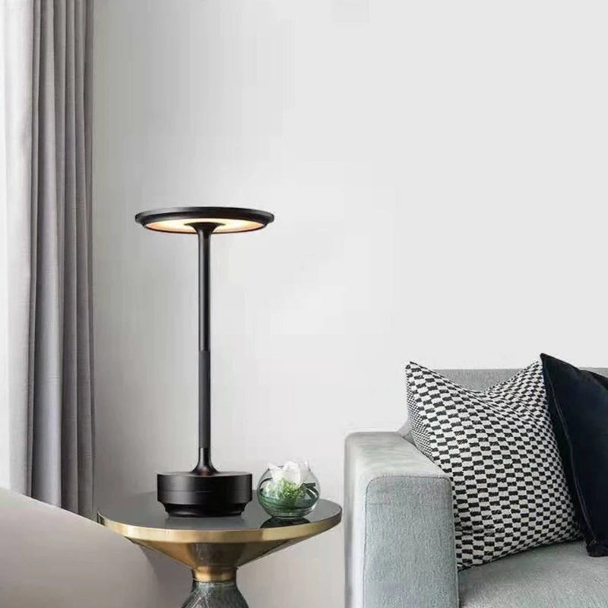 Modern black table lamp on a side table with a gray sofa and decorative pillows in a living room setting.