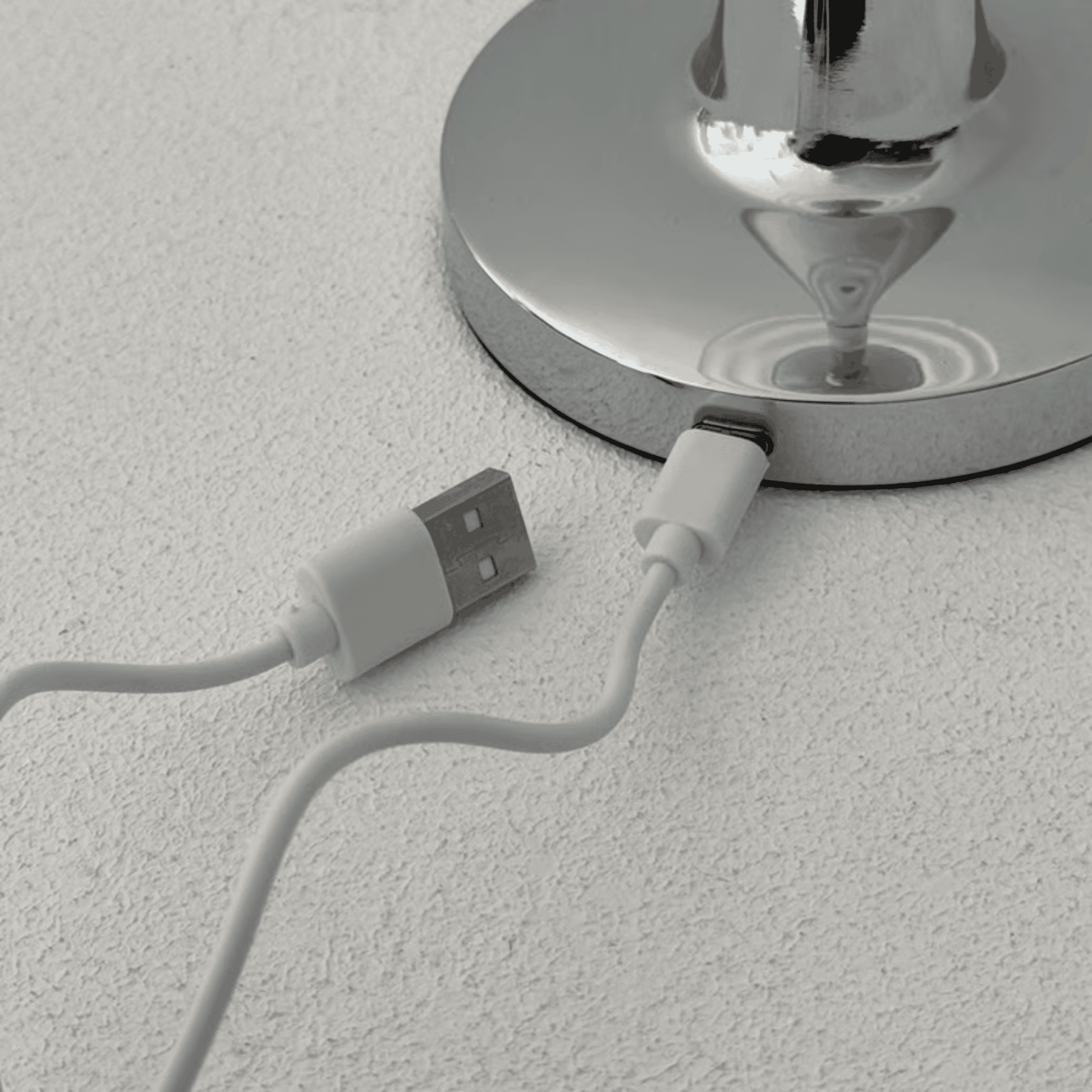 USB cable plugged into a metallic faucet on a textured surface