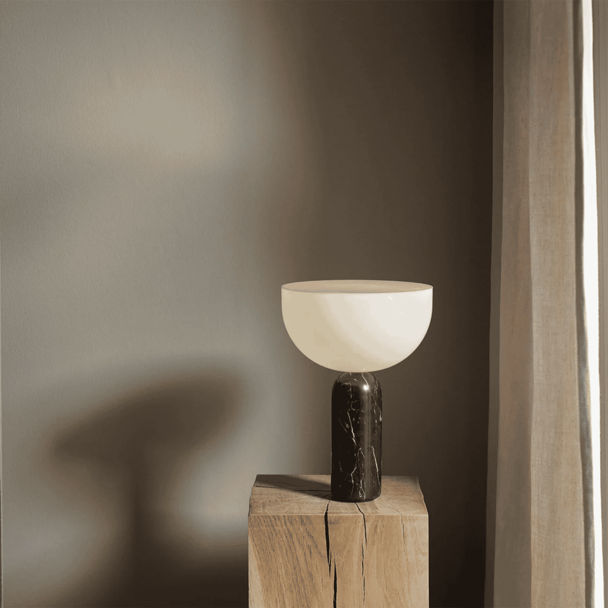 Minimalist table lamp with marble base on a wooden block against a neutral wall.