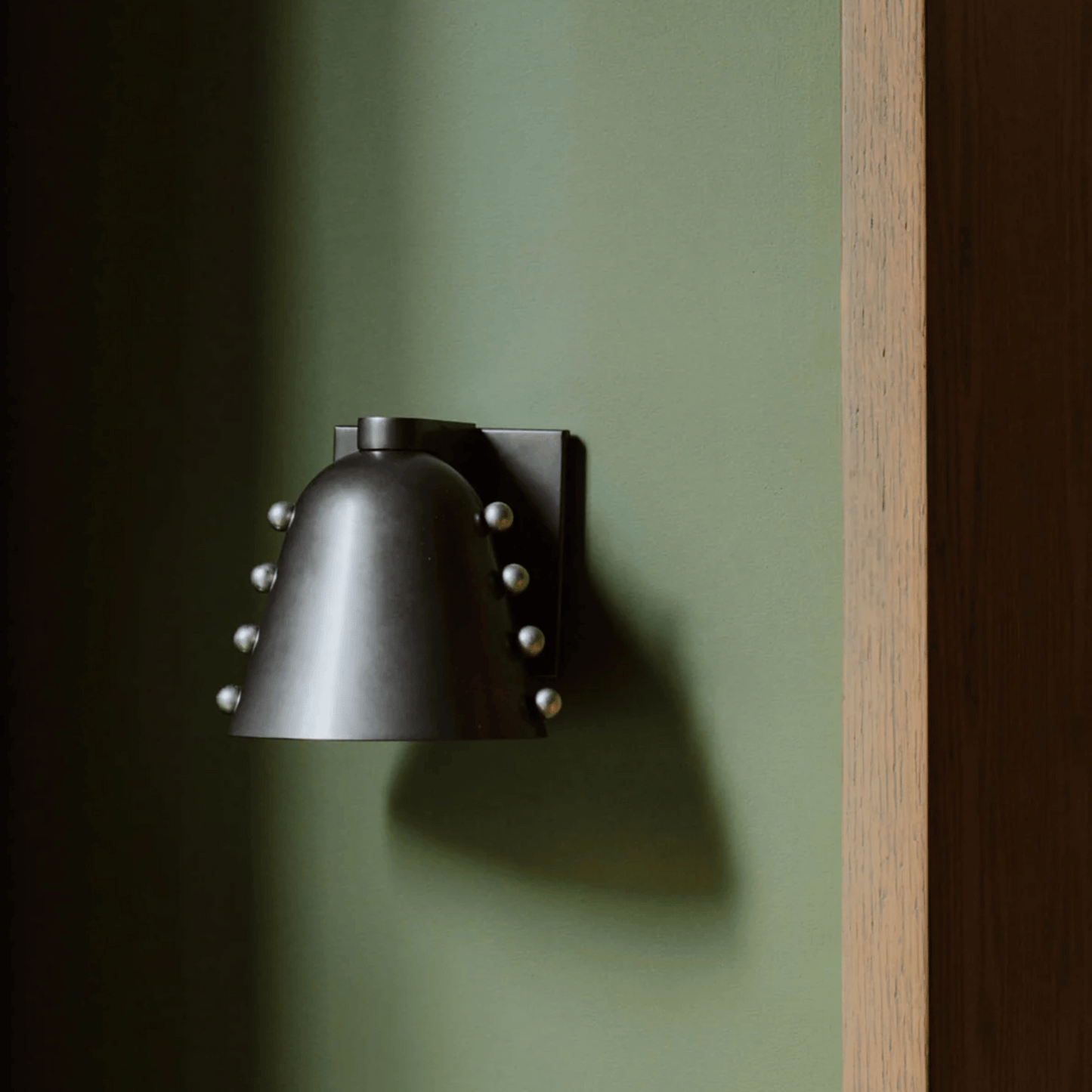 Black wall-mounted light fixture on a green wall with a wooden frame.