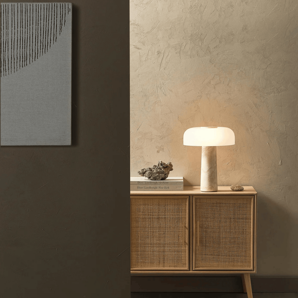 Nest table lamp on a wooden cabinet against a textured wall with abstract art.