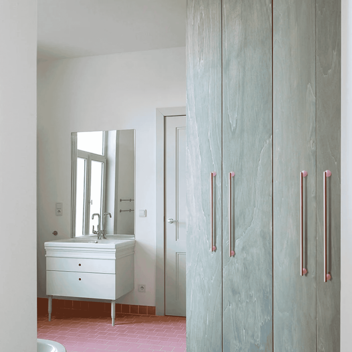 Bathroom with a vanity and mirror, partially obscured by a wooden wardrobe with pink handles.