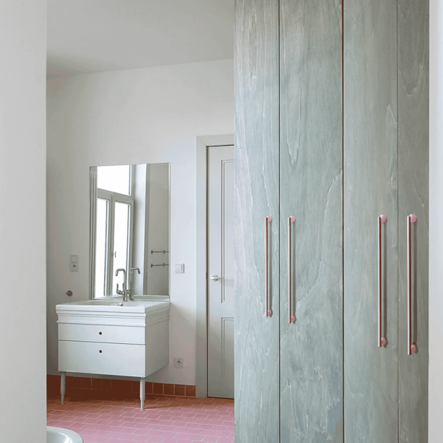 Bathroom with a vanity and mirror, partially obscured by a wooden wardrobe with pink handles.