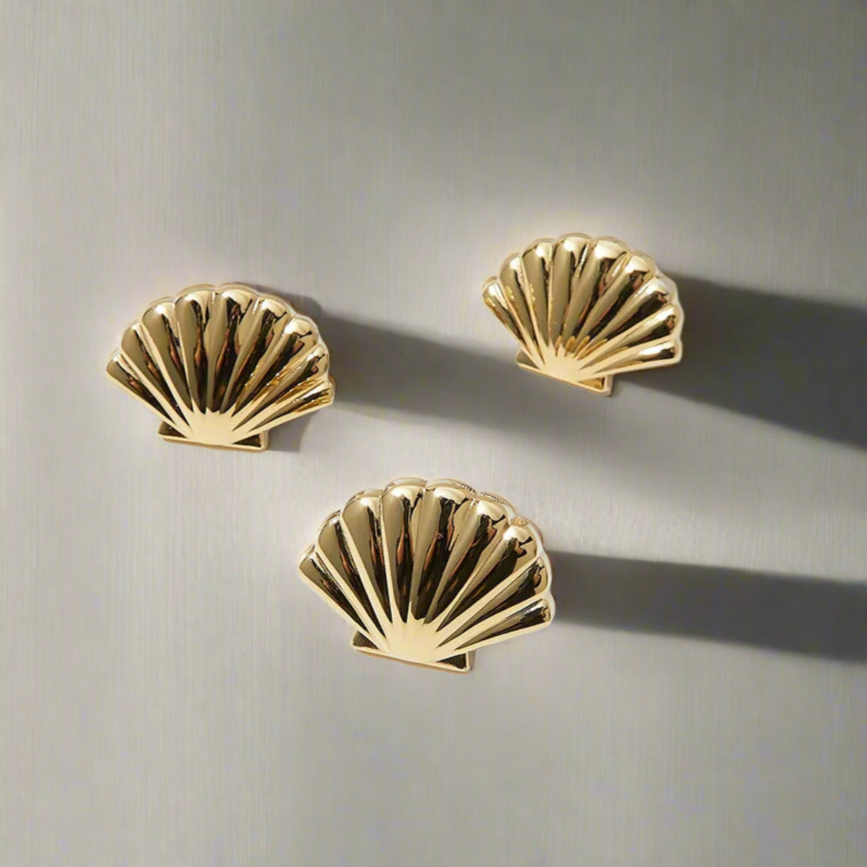 Three gold shell-shaped earrings on a white background