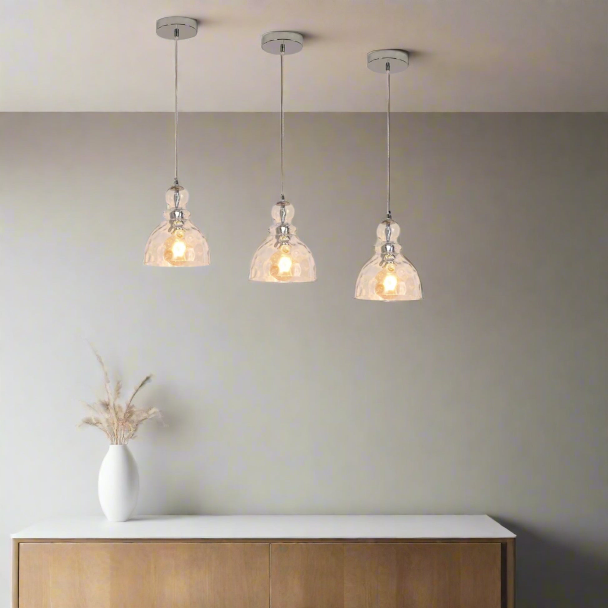Modern kitchen with white countertops, pendant lights, and a view of greenery outside.