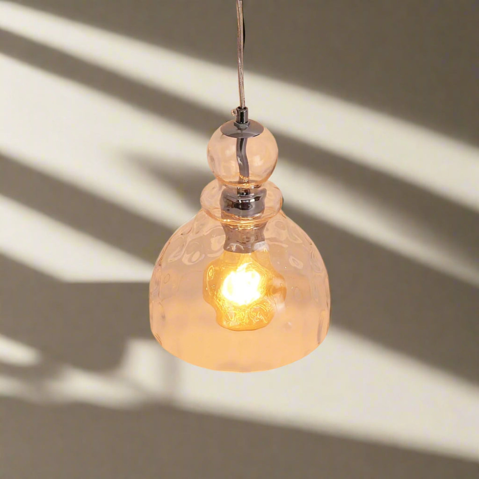 Clear glass pendant light with a glowing bulb against a neutral background