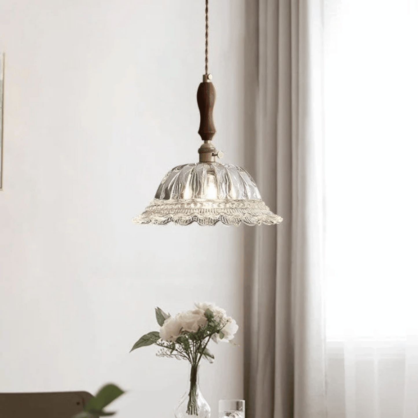 Glass pendant light fixture with wooden accent hanging above a table with flowers.