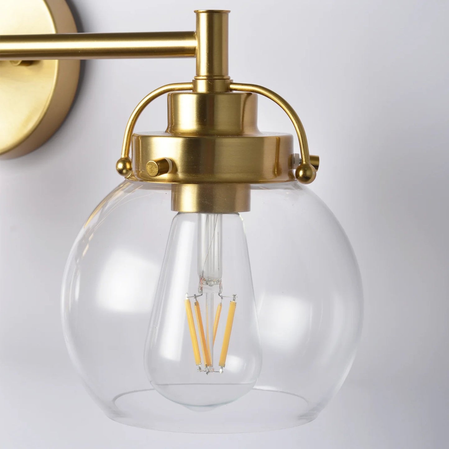 Wall-mounted light fixture with gold finish and clear glass shade on a white background