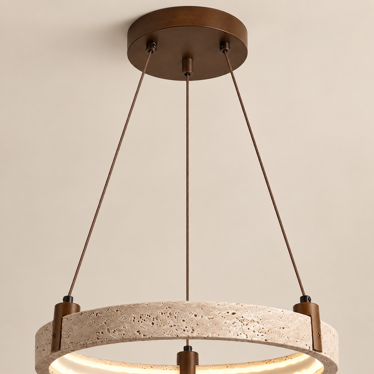 A modern pendant light fixture with a textured stone ring and a dark bronze metal frame, suspended by three cables from a matching circular ceiling canopy against a plain beige wall.