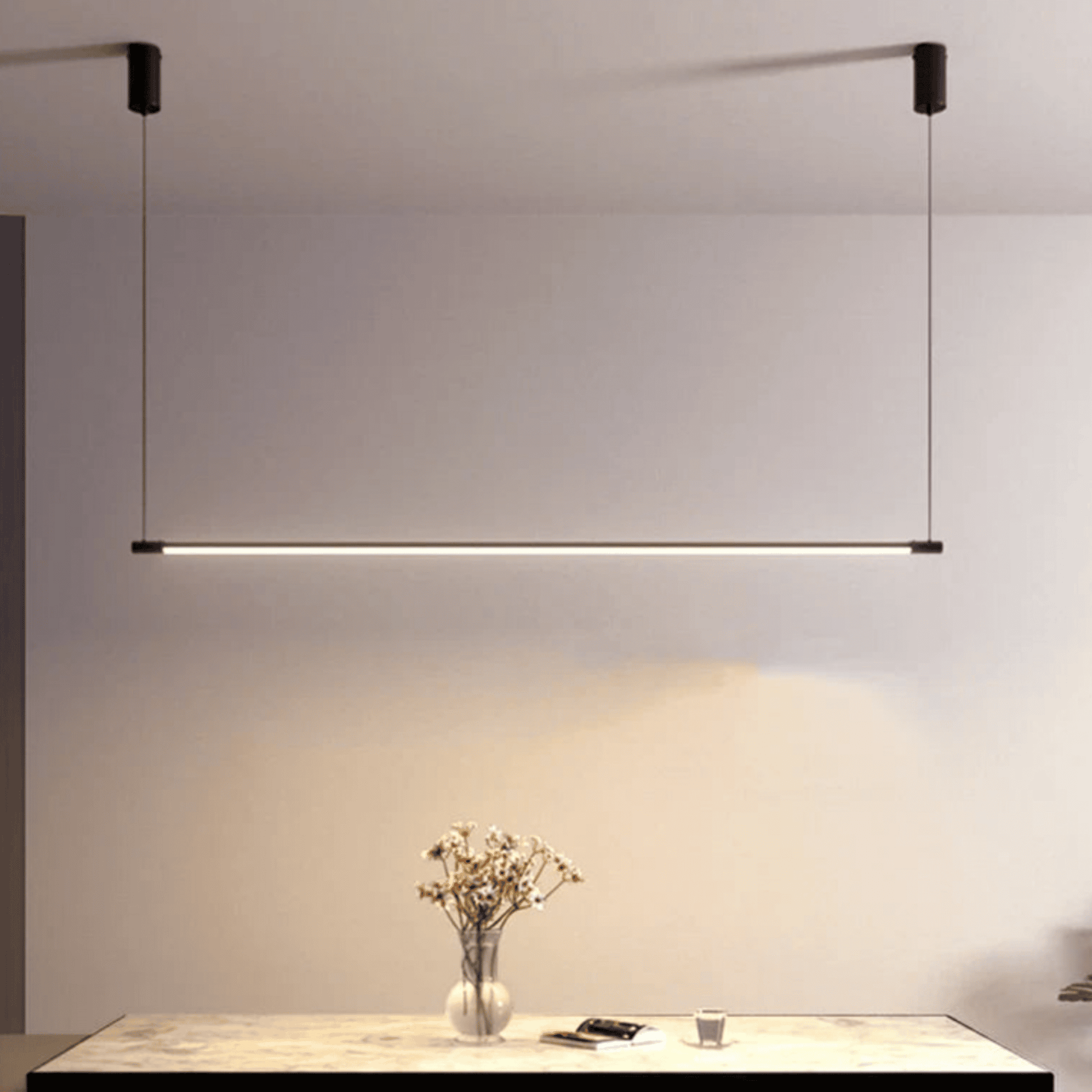 Modern pendant light hanging above a table with a vase of flowers and remote control.
