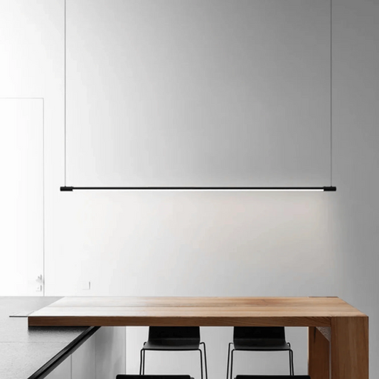 Modern dining table with chairs under a long pendant light in a minimalistic setting.