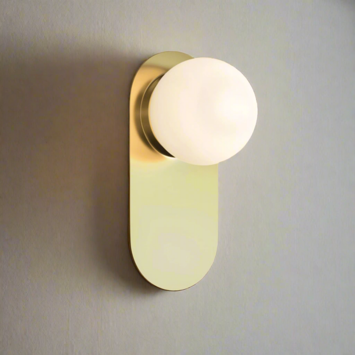 Modern wall light fixture with gold finish and white glass shade on a beige background