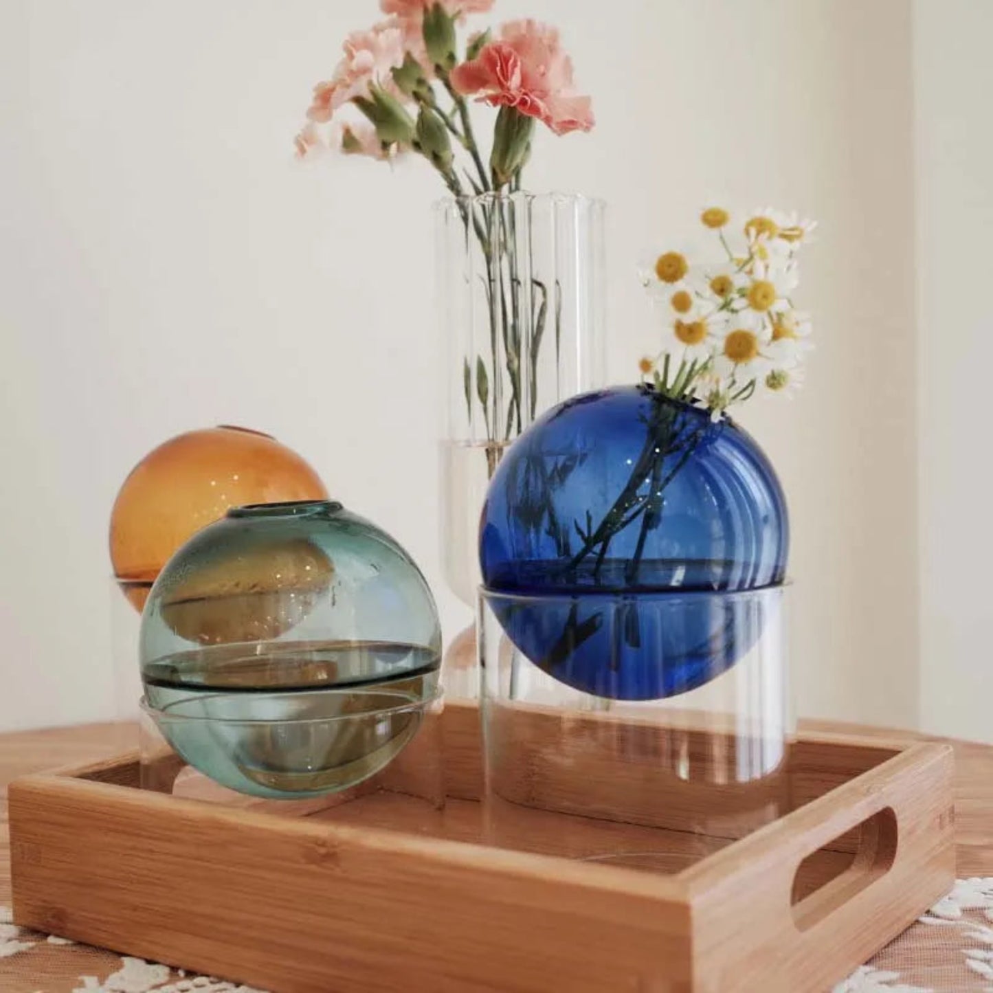 Decorative glass spheres on a wooden tray with flowers in the background