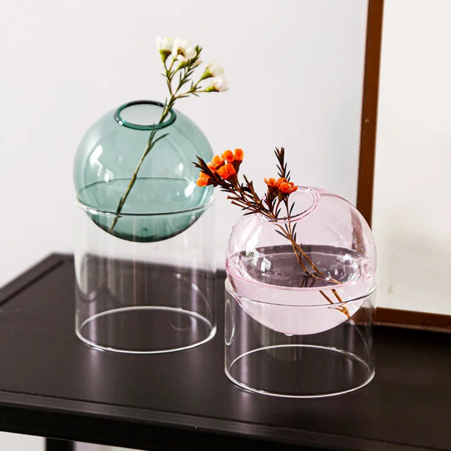 Two glass vases with floral arrangements on a dark surface.