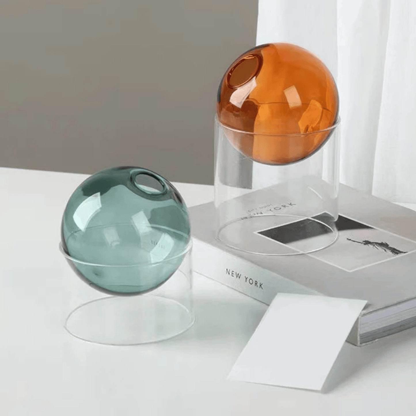 Two spherical glass objects on a surface with a book and paper in the background.