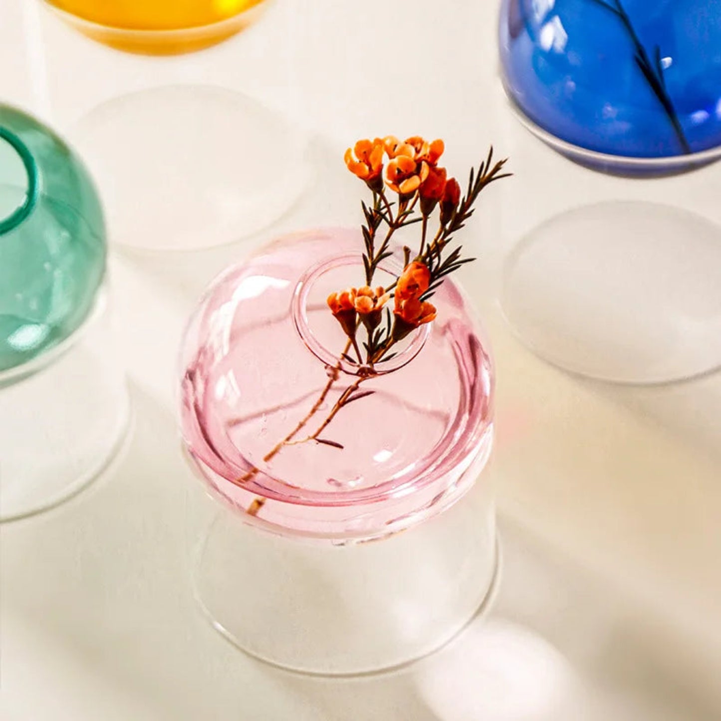 Small pink glass vase with dried flowers on a white surface