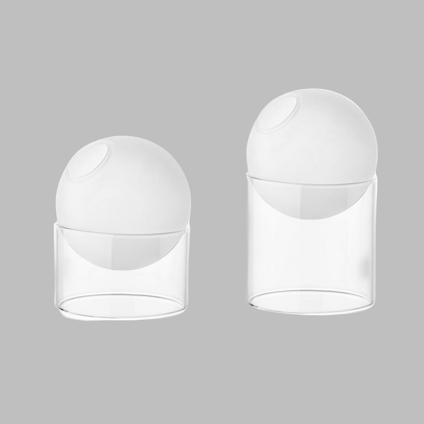 Two white spherical objects with clear cylindrical bases on a white background