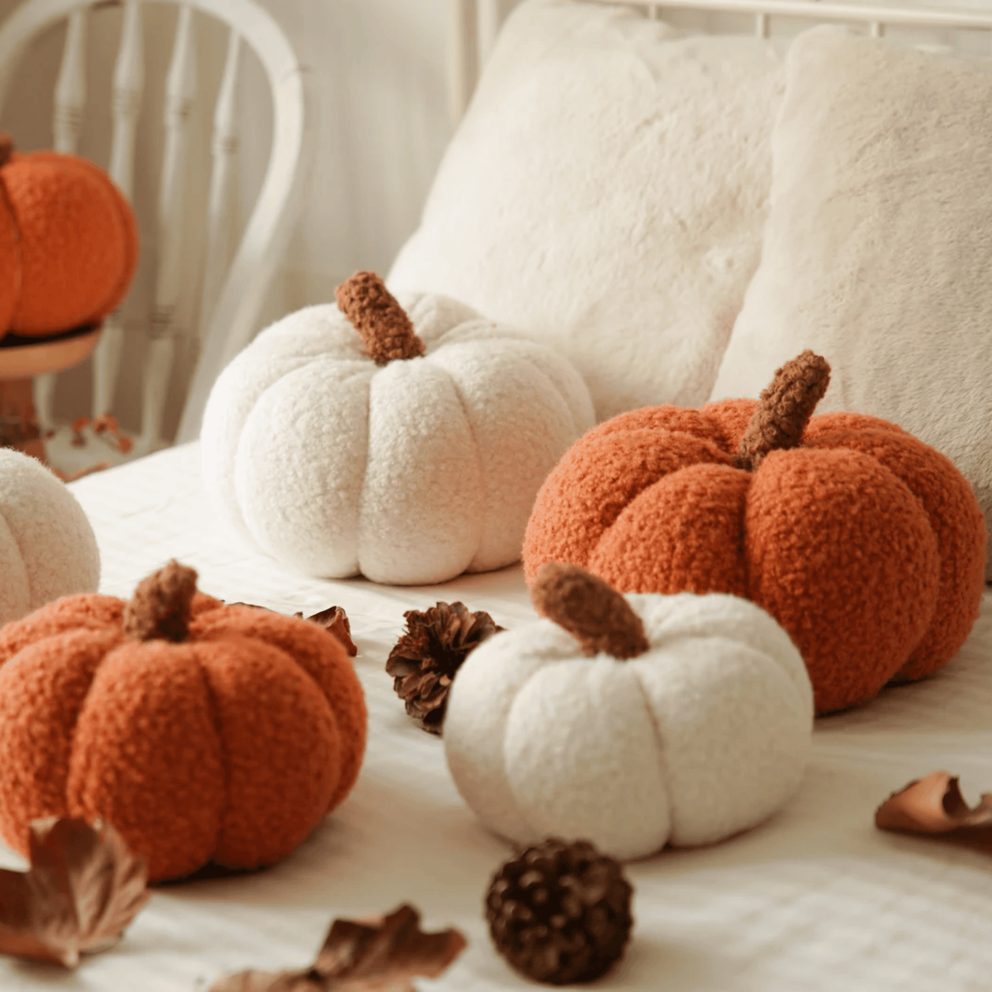 Decorative pumpkins in orange and white on a soft surface with pinecones.