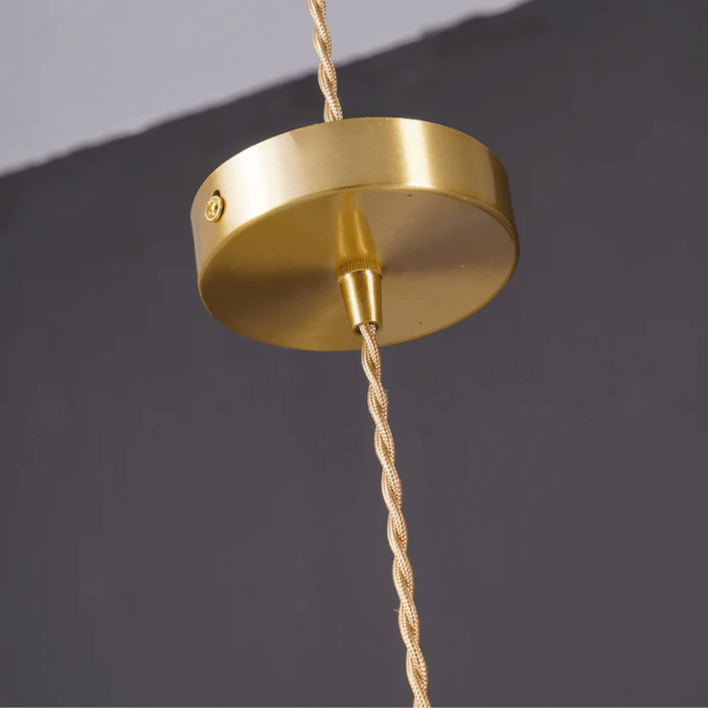 Gold ceiling light fixture with braided cable against a dark background