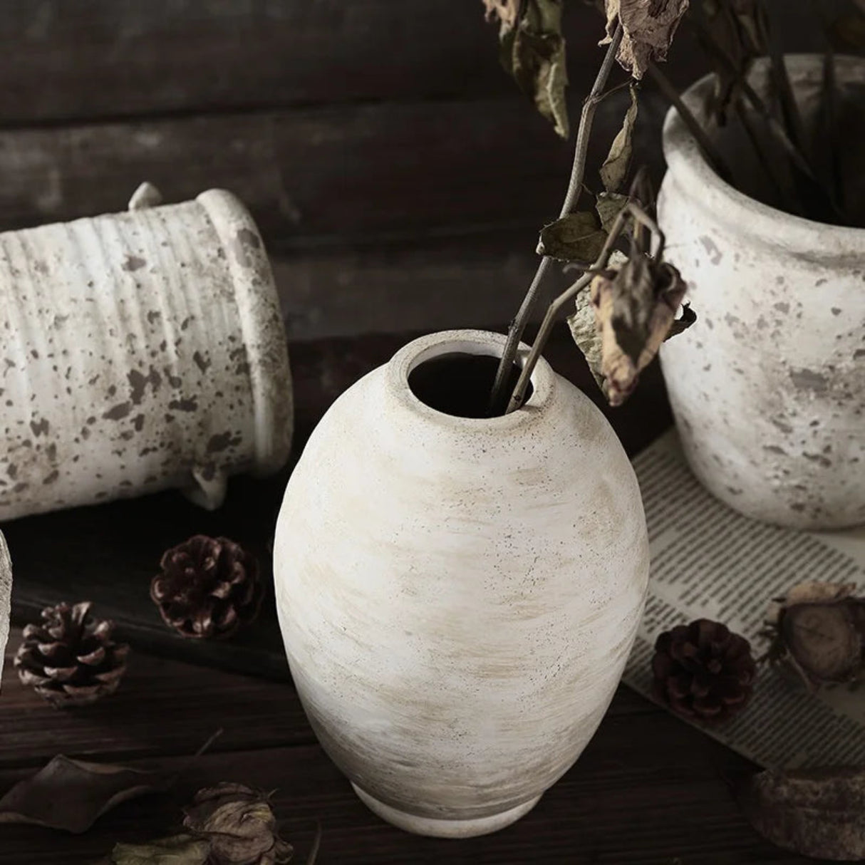 White textured vase with dried plant on a dark surface