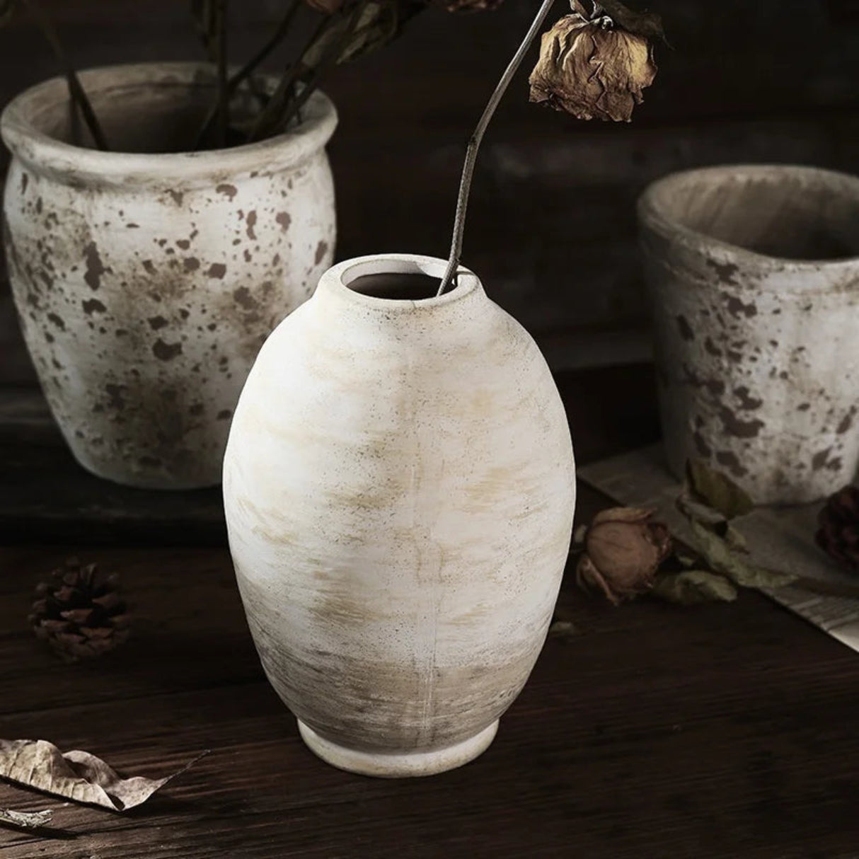 White ceramic vase on a dark surface with other ceramic pots in the background