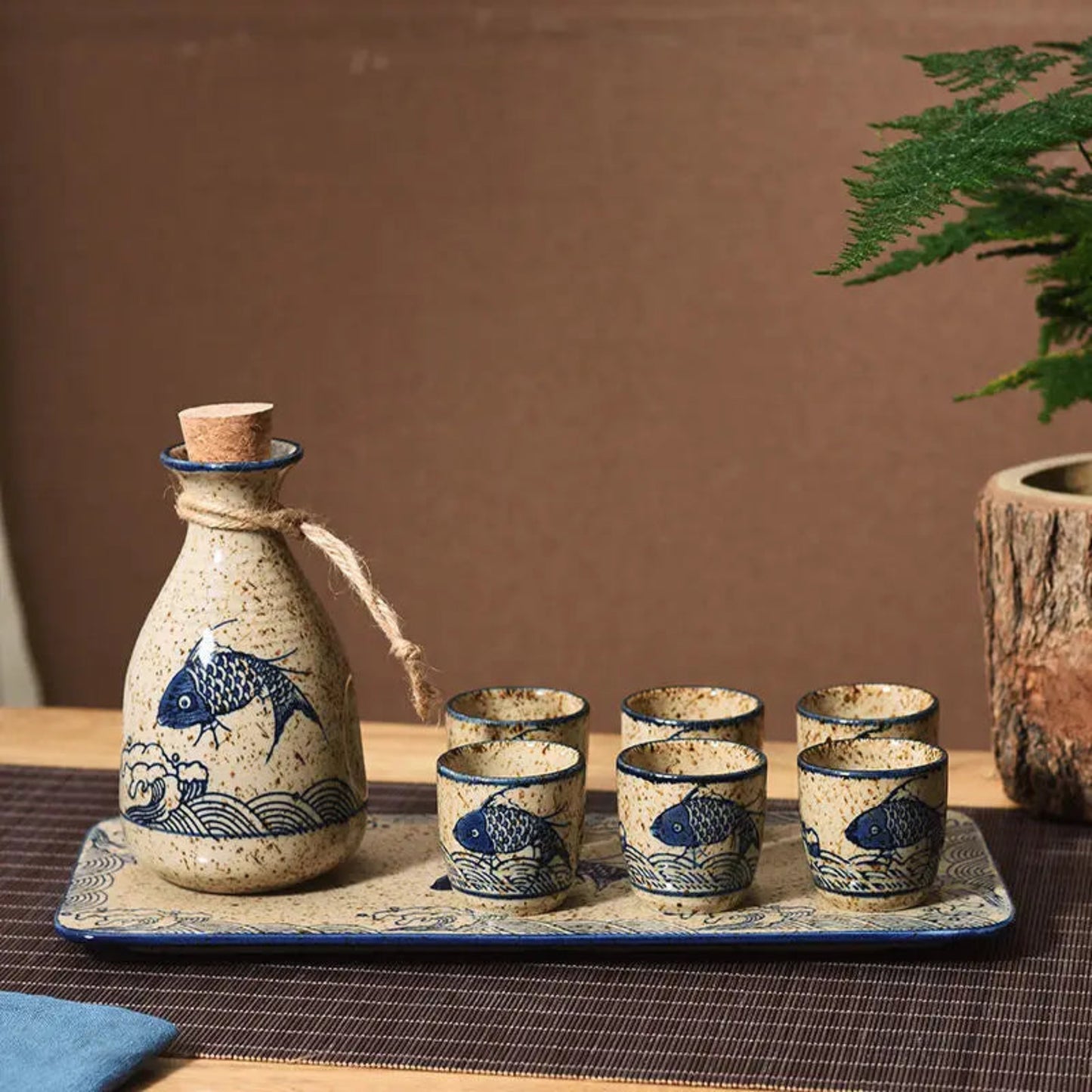 Ceramic sake set with bottle and four cups on a tray, featuring fish designs, against a brown background.