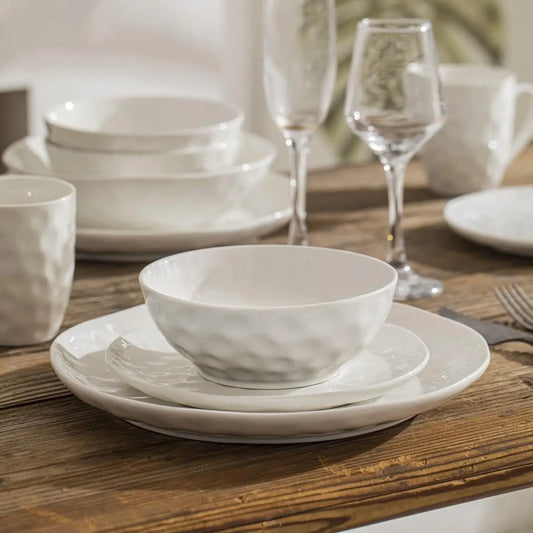 White ceramic dinnerware set on a wooden table with glasses in the background