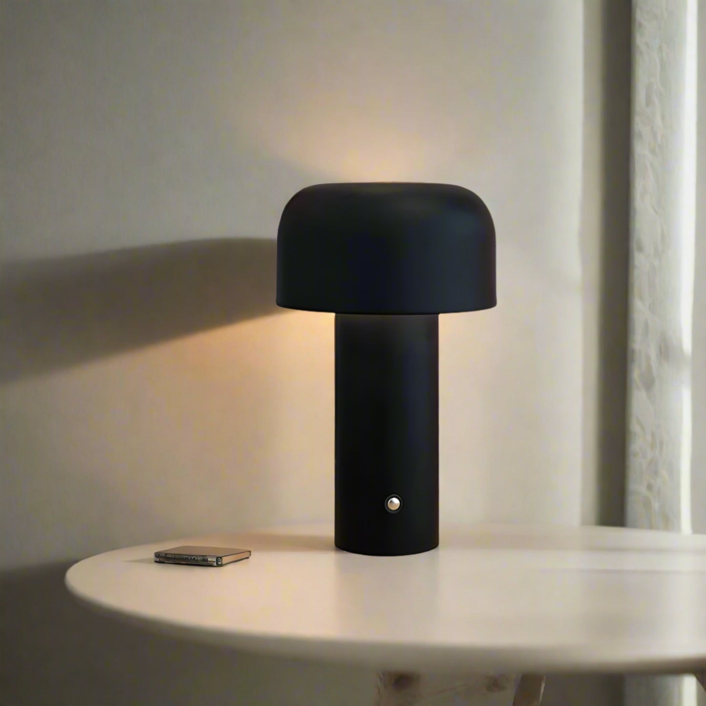 Black mushroom-shaped table lamp on a wooden surface with books and a decorative poster in the background.