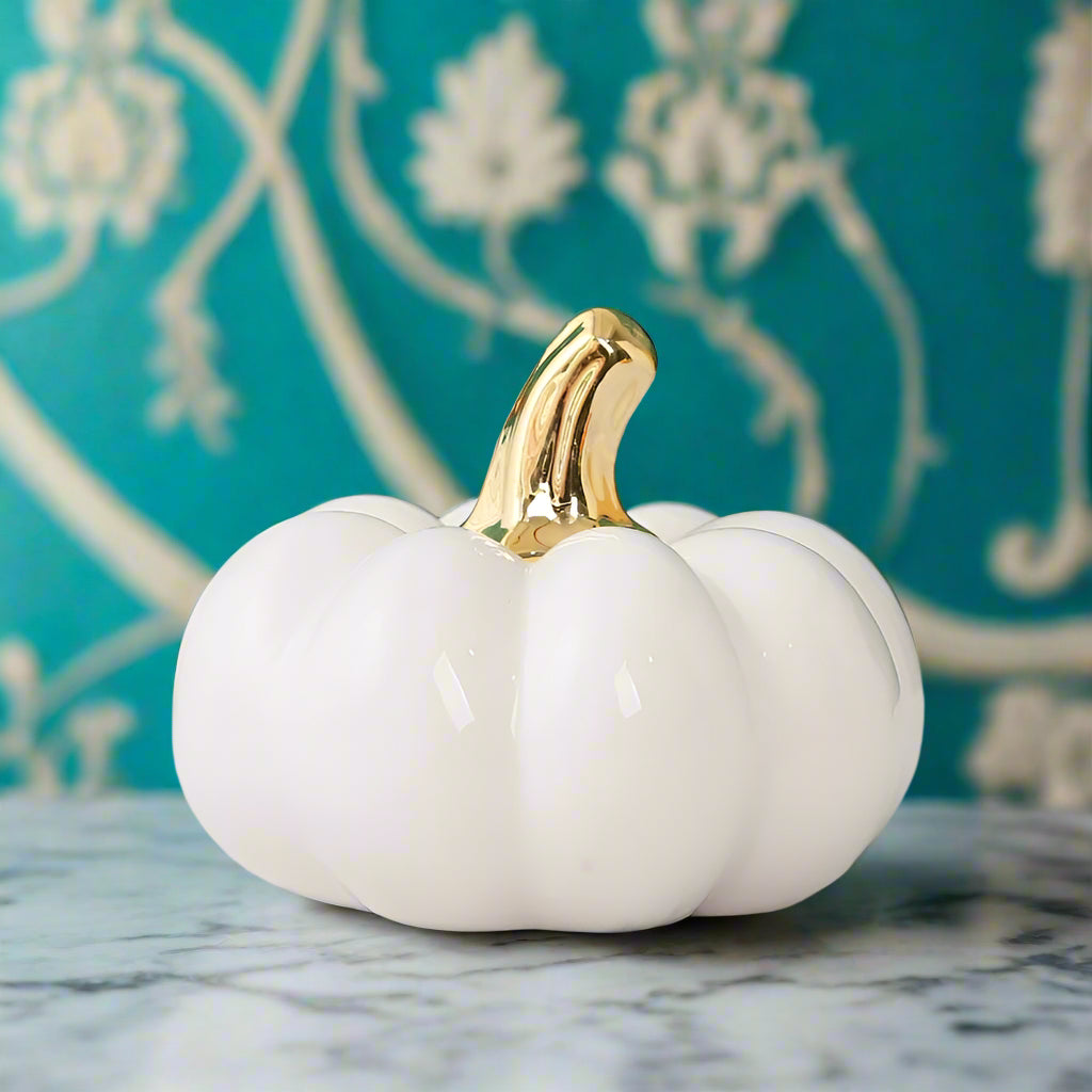 White pumpkin with a gold stem on a light surface with a blurred background