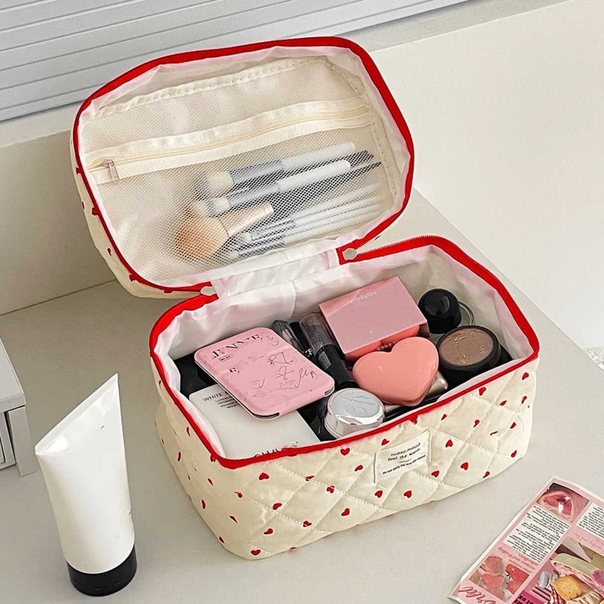 Makeup bag with heart patterns containing various cosmetic items on a light surface.