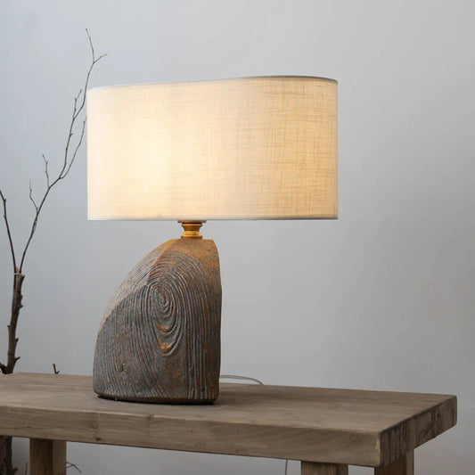 Table lamp with wooden base and beige shade on a wooden table against a gray background