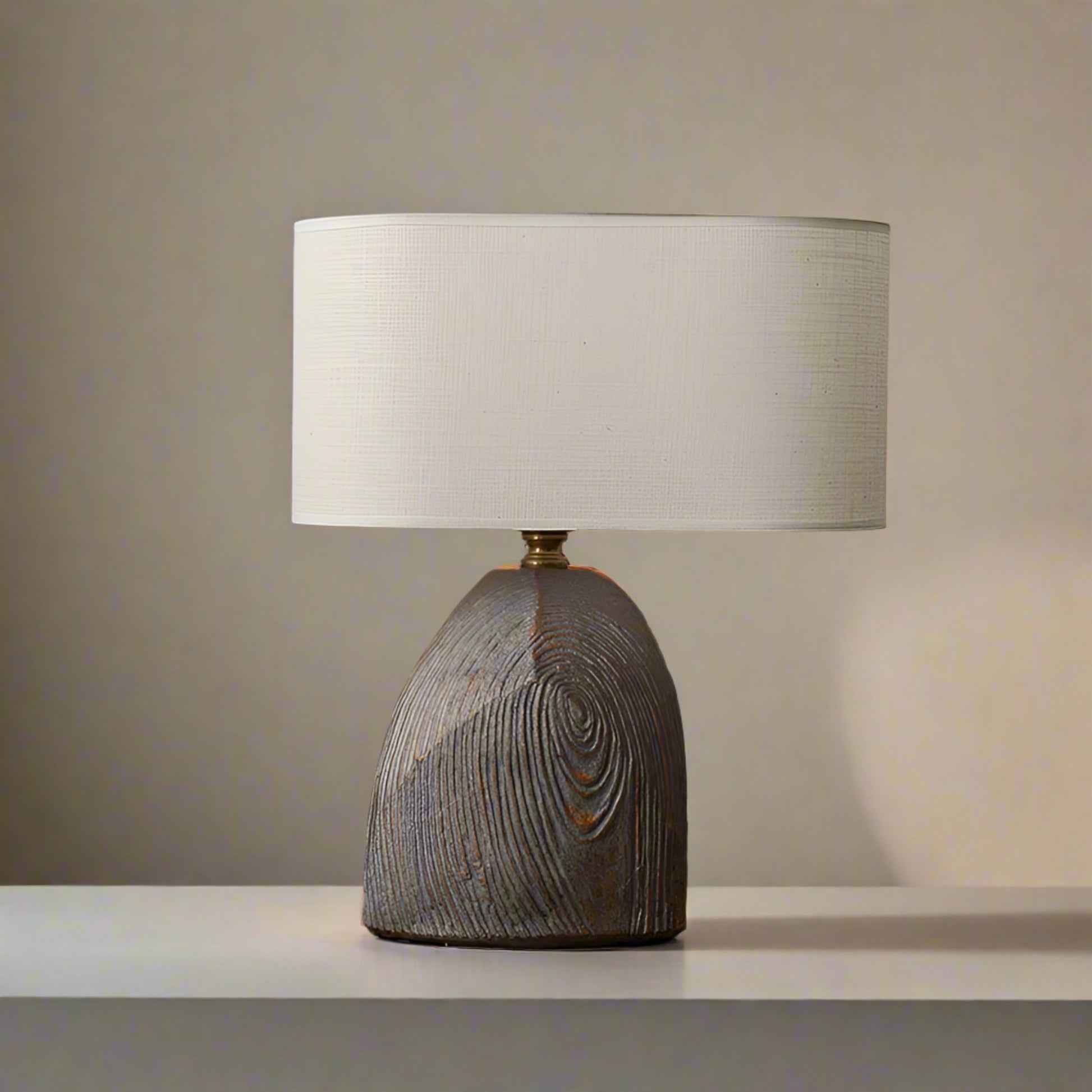 Table lamp with wooden base and beige shade on a wooden table against a gray wall