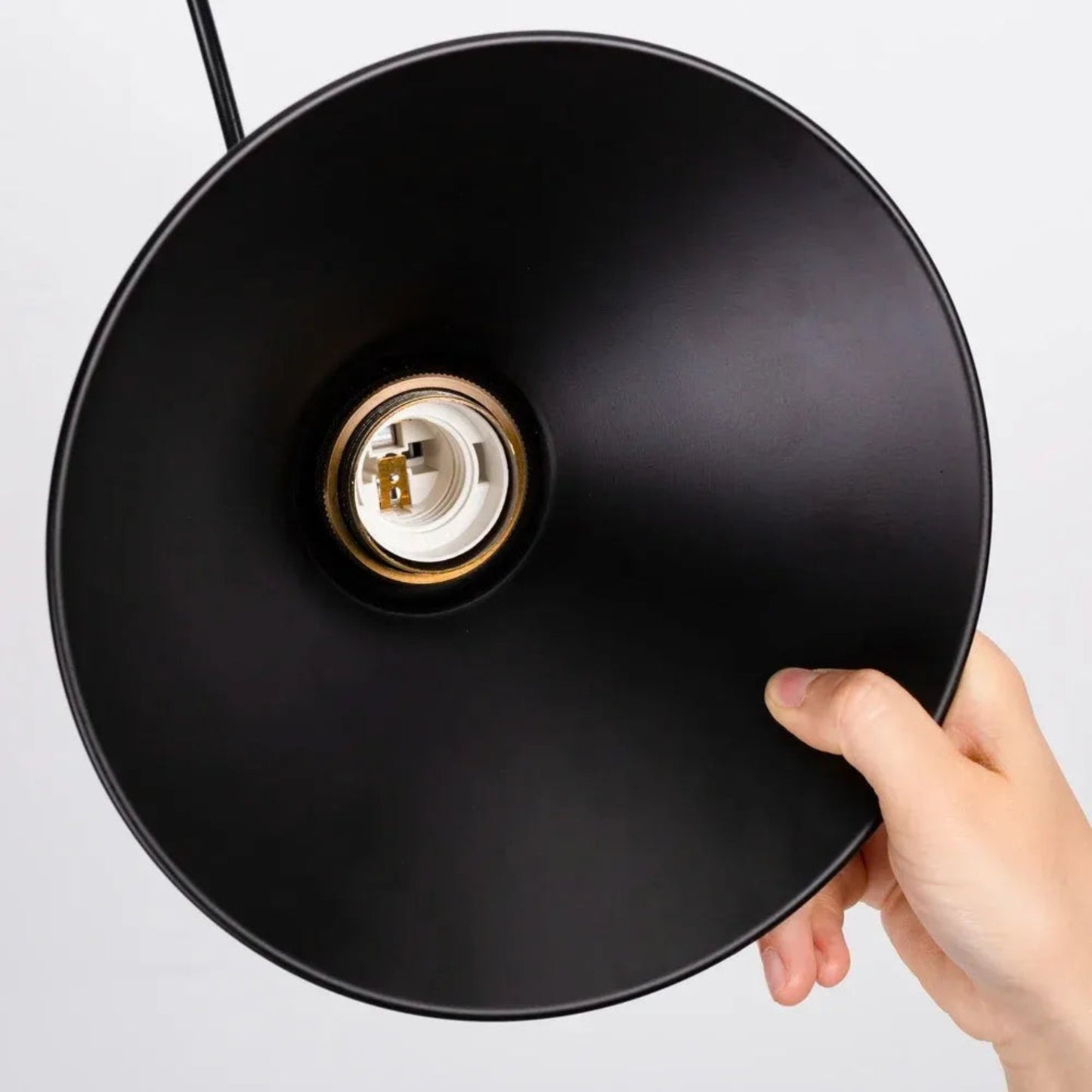 Hand holding a black lampshade with a visible light bulb socket on a white background