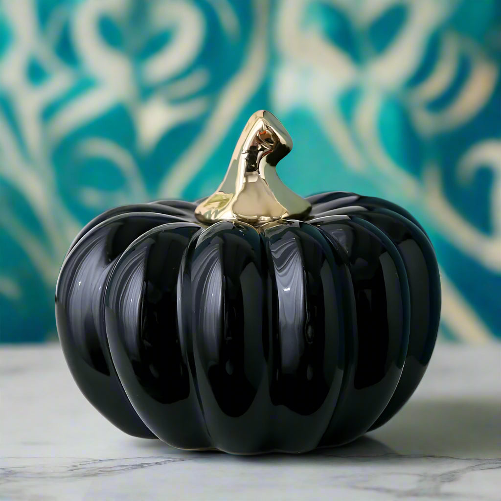 Decorative black pumpkin with gold top on a light surface