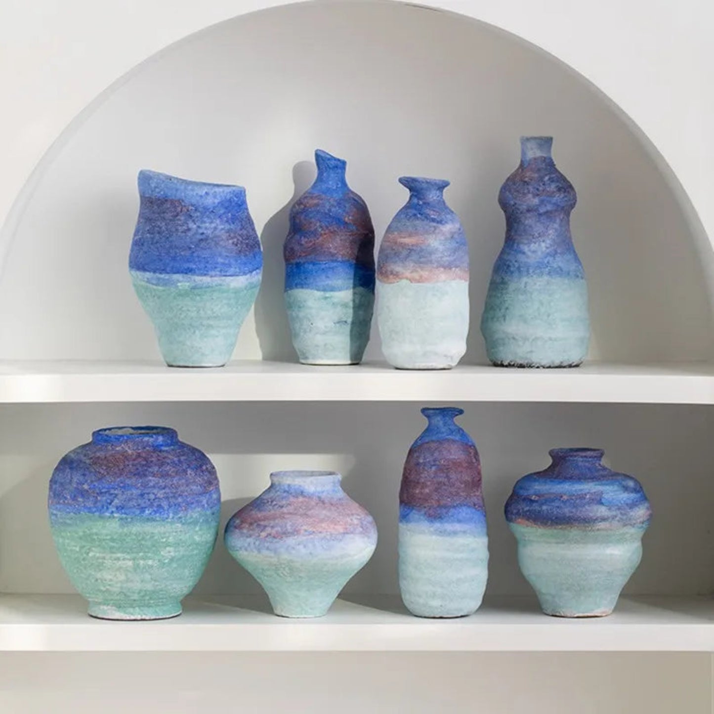 Set of ceramic vases with blue and green gradient on a white shelf.