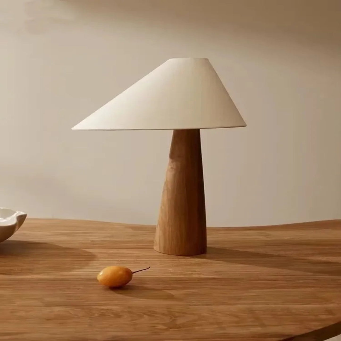Table lamp with wooden base and white shade on a wooden table.