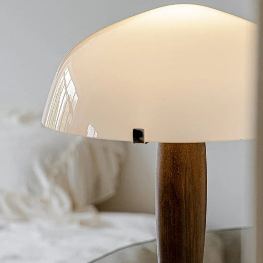 Table lamp with wooden base and white glass shade on a blurred background